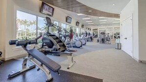 A gym with cardio machines, a bench press, and a wall-mounted TV. - Beautiful newly furnished Villa in a resort community with tons of amenities (Naples)