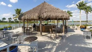 A thatched-roof outdoor seating area with tables and chairs, a bar, and a view of the water. - Beautiful newly furnished Villa in a resort community with tons of amenities (Naples)