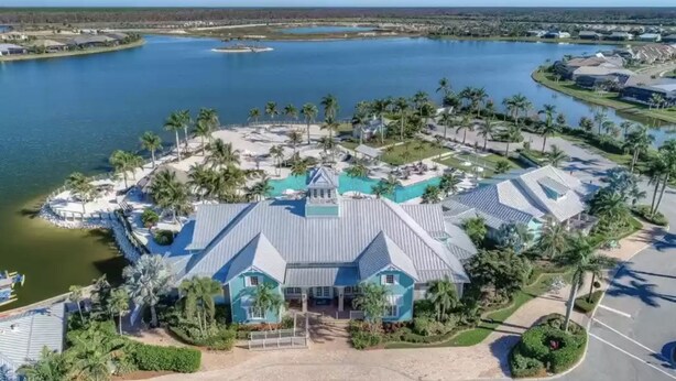 A large, single-story building with a blue roof, surrounded by palm trees and a lake. - Beautiful newly furnished Villa in a resort community with tons of amenities (Naples)