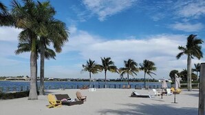 A beach with sun loungers and palm trees, a clear sky, and a view of the water. - Beautiful newly furnished Villa in a resort community with tons of amenities (Naples)