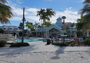 A resort with a swimming pool, palm trees, and a signpost with various directions.