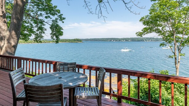 A wooden deck with a table and chairs overlooking a lake with boats. - Bay-View. Waterfront Log cabin on the bay. Pet Friendly.  (Harpswell)