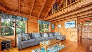 A cozy cabin interior with a wooden ceiling, a gray sofa, a wooden coffee table, and large windows offering a view of the outdoors. - Bay-View. Waterfront Log cabin on the bay. Pet Friendly.  (Harpswell)