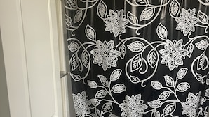 Ein Badezimmer mit Duschvorhang mit Blumenmuster, Toilette und Teppich mit Streifen.
