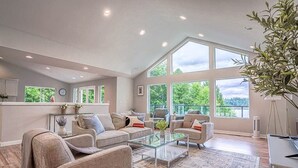 A spacious living room with large windows, a glass coffee table, and a comfortable seating area. - Modern Shelton Waterfront:Hot Tub,Games&Serenity (Shelton)