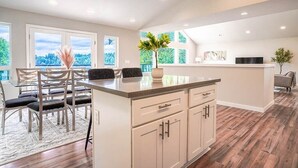 A modern kitchen with a central island, white cabinetry, and a dining area with chairs and a table. - Modern Shelton Waterfront:Hot Tub,Games&Serenity (Shelton)