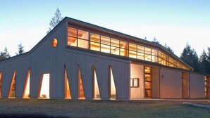 A modern building with large windows and a sloped roof, situated near a body of water. - Modern Shelton Waterfront:Hot Tub,Games&Serenity (Shelton)