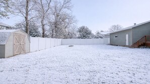 Un patio nevado con un cobertizo de madera, una cerca blanca y una casa.