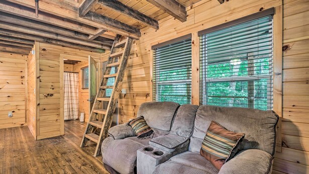 A wooden cabin interior with a sofa, a ladder, and a window with blinds. - Peaceful Decatur Cabin w/ Grill & Fire Pit! (Decatur)