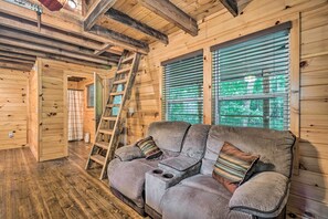 A wooden interior with a sofa, a ladder, and a window with blinds. - Peaceful Decatur Cabin w/ Grill & Fire Pit! (Decatur)