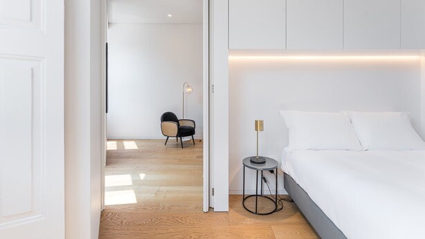 A modern bedroom with a large bed, a bedside table, a floor lamp, and a chair. - GuestReady - Mompilher Apartments (Porto)