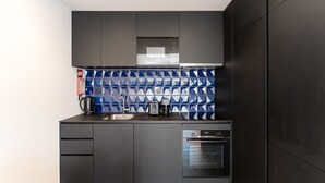 A modern kitchen with dark cabinetry, a stainless steel sink, a kettle, a toaster, and a built-in oven. - GuestReady - Mompilher Apartments (Porto)