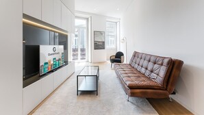 A modern living room with a leather sofa, a glass coffee table, and a mounted TV displaying 'GuestReady'. - GuestReady - Mompilher Apartments (Porto)