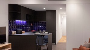 Eine moderne Küche mit dunklen Schränken, einer zentralen Kochinsel mit Sitzgelegenheiten und einem Essbereich mit Sofa und Fernseher.