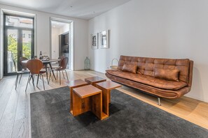 A modern living room with a leather sofa, wooden coffee table, and dining area with chairs. - GuestReady - Mompilher Apartments (Porto)