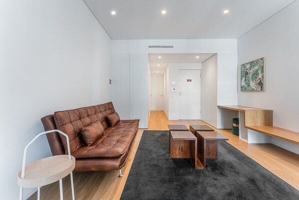 A modern living room with a brown leather sofa, a wooden coffee table, and a minimalist design. - GuestReady - Mompilher Apartments (Porto)