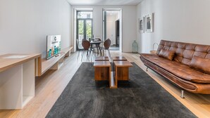 A modern living room with a leather sofa, a coffee table, and a dining area with chairs and a table. - GuestReady - Mompilher Apartments (Porto)