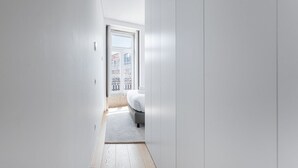 A narrow hallway leading to a bedroom with a large window, a door, and a small rug on the floor. - GuestReady - Mompilher Apartments (Porto)