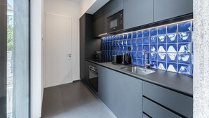 A modern kitchen with dark grey cabinets, a stainless steel sink, and a blue-tiled backsplash. - GuestReady - Mompilher Apartments (Porto)