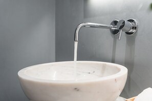 A white ceramic sink with a chrome faucet against a grey wall.