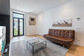 A modern living room with a leather sofa, a glass coffee table, and a painting of giraffes on the wall. - GuestReady - Mompilher Apartments (Porto)