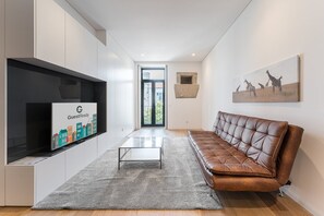 A modern hotel lobby with a leather sofa, a glass coffee table, a flat-screen TV displaying 'GuestReady', and a framed giraffe painting on the wall. - GuestReady - Mompilher Apartments (Porto)