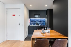 A modern kitchen with a built-in microwave, a sink, and a blue tiled backsplash. There is a wooden table with chairs in the foreground.