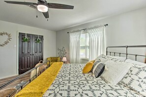 Een slaapkamer met een bed, een plafondventilator, een deur versierd met kransen, en een raam met gordijnen.
