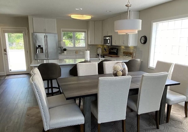 A modern kitchen with white cabinetry, a dining table with cushioned chairs, and a pendant light.