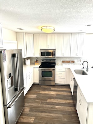 Una cocina moderna con electrodomésticos de acero inoxidable, armarios blancos y piso de madera.