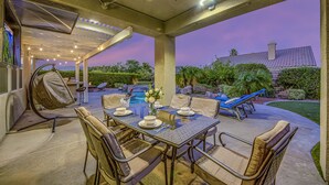 An outdoor patio with a table set for dining, a swing chair, and a pool in the background. - Feel yourself at home !!! (Indio)