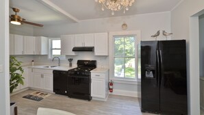 A modern kitchen with white cabinets, a black refrigerator, a gas stove, and a chandelier.