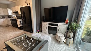 A modern kitchen with a black refrigerator, a dining table, and a large TV on a wooden cabinet.