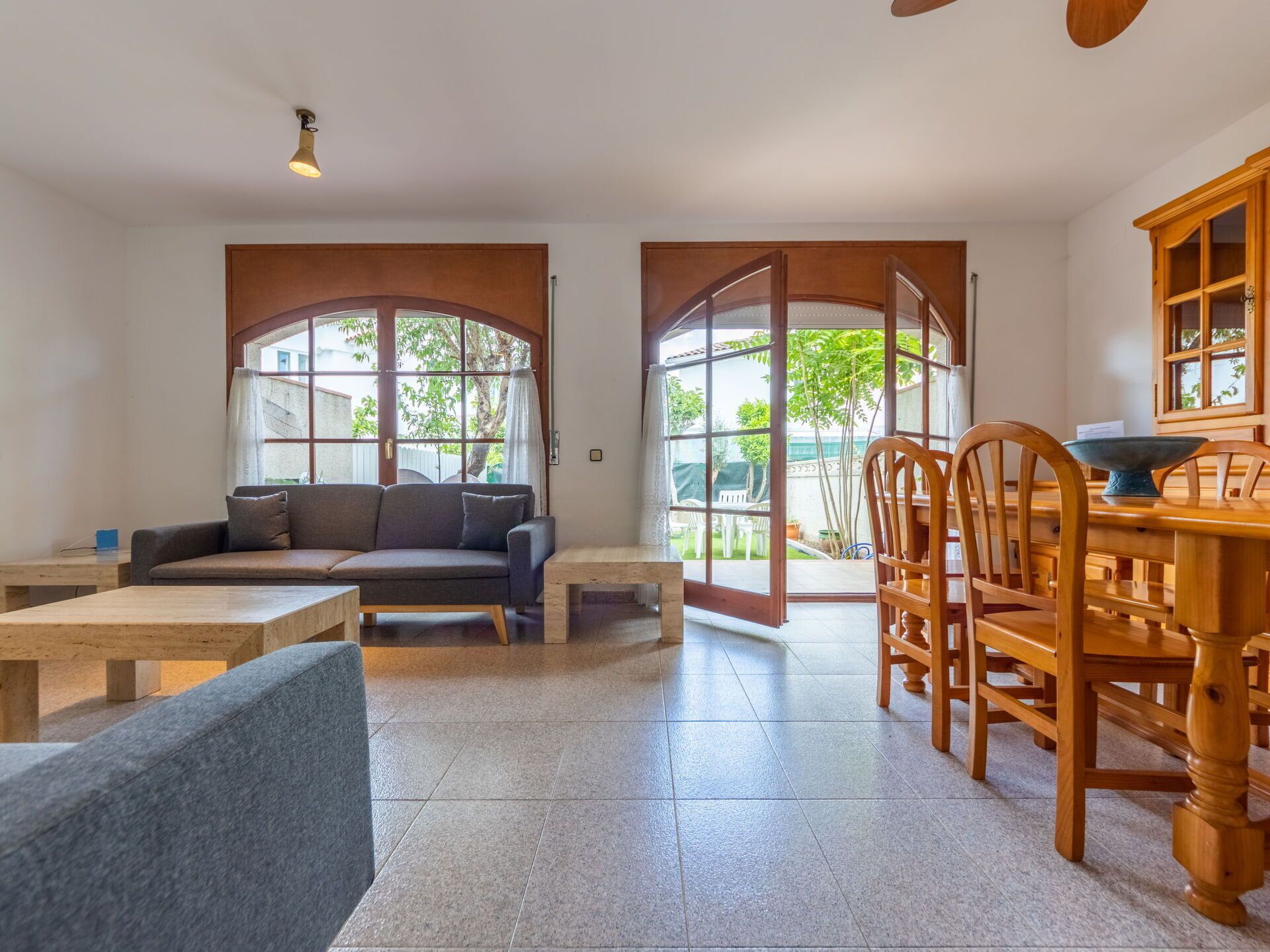 Uma sala de estar ampla, com sofá, mesa de jantar e cadeiras, e grandes janelas que oferecem luz natural.