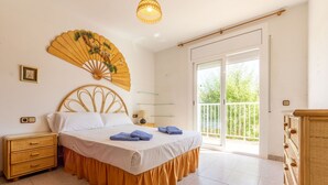 Ein Schlafzimmer mit Bett, Nachttisch, Kommode, Wandventilator und einem Balkon mit Geländer.