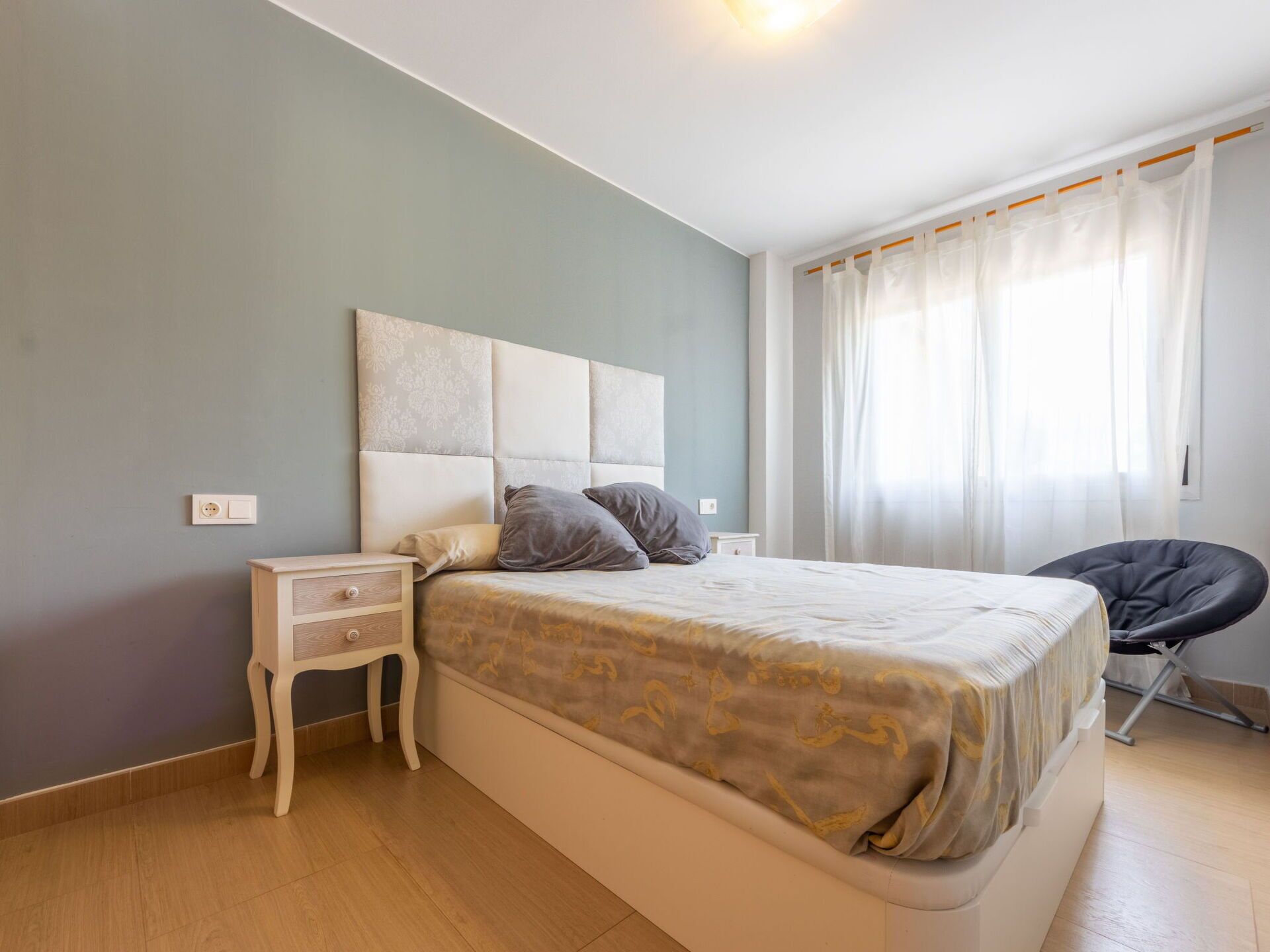 Une chambre à coucher avec un lit, des tables de chevet, une chaise et une fenêtre avec des rideaux.
