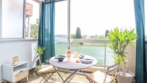 A balcony with a table set for two, a potted plant, and a view of a body of water.