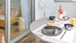 A dining table set with plates, cutlery, glasses, and a bottle of wine, with a fan and a window in the background.