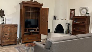 A living room with a grey sofa, wooden cabinet, TV, fireplace, and a ceiling with exposed beams.