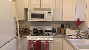 A compact kitchen with white cabinets, a microwave, a stove, and a toaster. There is a red and white checkered towel hanging on the oven handles.