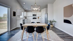 Una cocina moderna con armarios blancos, una mesa de comedor de madera con sillas negras y una lámpara colgante.