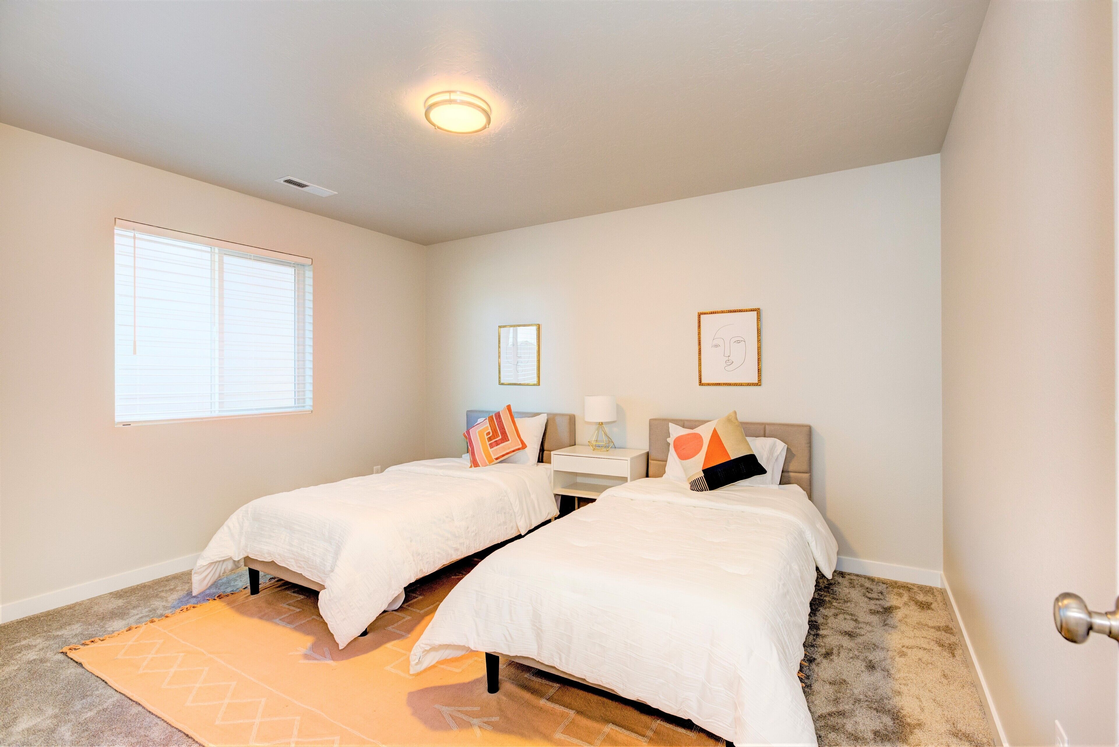 A bedroom with two beds, a window, a nightstand, and a wall-mounted artwork.