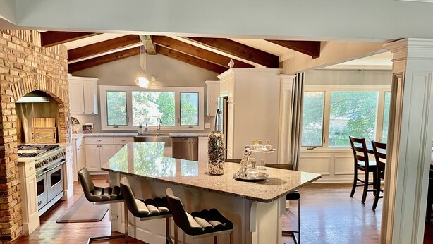 A modern kitchen with a large island, bar stools, a brick oven, and a view of the outdoors.