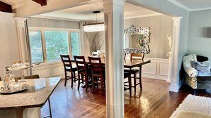 A spacious dining area with a wooden table and chairs, a chandelier, and a view of the outdoors through large windows.