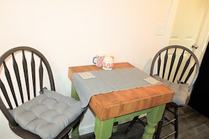Un petit coin repas avec deux chaises et une table, une tasse posée sur la table, et une porte à l’arrière-plan.