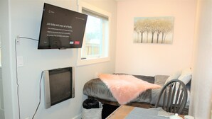 Un dormitorio con cama, televisor montado en la pared, ventana y un cuadro colgado.