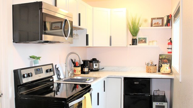 Cocina compacta con estufa, microondas, fregadero y lavavajillas. Hay un refrigerador pequeño, una cafetera y una planta en la encimera.