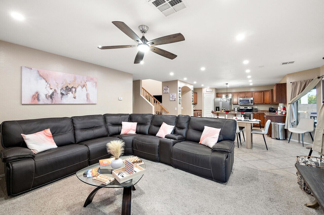 A modern living room with a sectional sofa, a glass coffee table, and a ceiling fan.