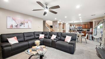 A modern living room with a sectional sofa, a glass coffee table, and a ceiling fan.