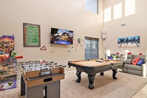 A room with a foosball table, pool table, and a sofa with colorful cushions. - Desert Oasis Amazing Pool/Waterfall/Firepit/Office (Casa Grande)